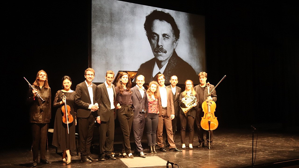 Group of Musicians at the Sprudeling Fountain in front of a photo of Robert Kahn